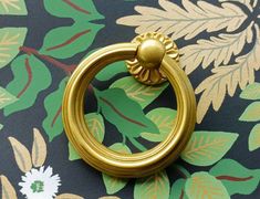 a close up of a gold ring on a flowered wallpaper with green leaves