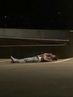 two people are laying on the ground in an empty parking lot at night, one person is holding his head