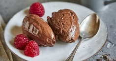 two scoops of chocolate ice cream on a plate with raspberries next to it