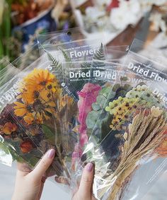 three packages of dried flowers are being held by someone's hand in front of them