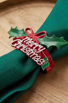 a green napkin with a red ribbon and holly decoration on it sitting on a wooden table