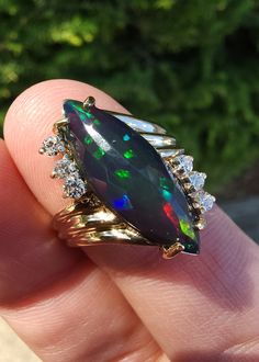 a woman's hand holding an opal and diamond ring