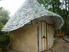 a house made out of plastic bottles in the middle of a park with a thatched roof