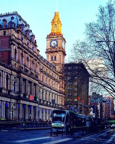 a bus driving down a street next to tall buildings with a clock tower in the background