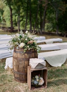 an old barrel with flowers and greenery on it is set up for a wedding ceremony