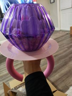 a purple vase sitting on top of a pink plate next to a person's hand