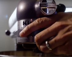 a close up of a person pressing something on top of a coffee machine with their hand