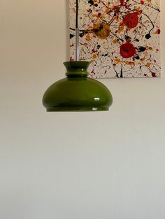 a green light hanging from the side of a white wall next to a painting on the wall