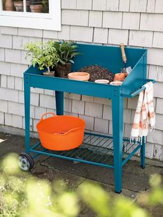 a blue potting bench with plants on it and an orange bucket in the foreground