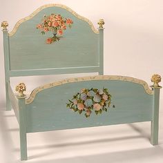 a blue painted bed with flowers on the headboard and foot board, against a white background