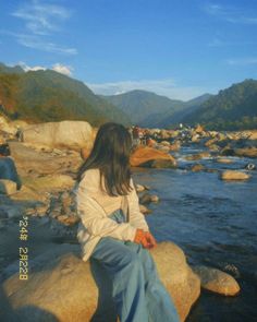 a woman sitting on top of a large rock next to a river filled with rocks