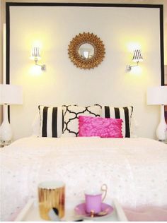 a white bed with black and white decor on the headboard, pink pillow, and coffee cup