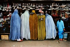 three people standing in front of a store with hats on their heads and shoes hanging from the ceiling