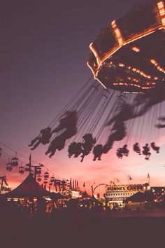 an amusement park at dusk with people riding on swings