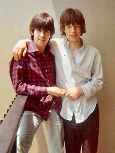 two men standing next to each other in front of a stair case with their arms around one another