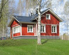 a red house sitting on top of a lush green hillside next to trees and grass