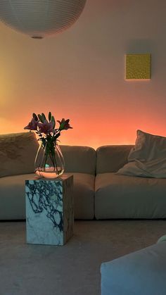 a vase with flowers sitting on top of a marble block in front of a couch