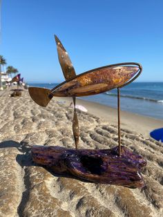 a piece of metal art sitting on top of a sandy beach next to the ocean