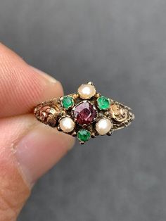 Delicate and Unique Victorian ring  Circa 1857 Many hallmarks - including 375 beautiful goldwork...a lost art! Hallmarked Birmingham 1857  3 Green Emeralds with surface wear  measuring approx. 2.25mm round faceted...sold to me as genuine but I think they may be paste (glass) which was customary in this era 3 pearls 3mm Genuine 4mm cushion cut garnet with surface crack...see photos 1 gram weight Natural patina ( antiquing) which could be cleaned but I leave the pieces as I find them unless they a Antique Gold Multi-stone Emerald Ring, Victorian Gold Emerald Ring, Antique Gold Emerald Ring With Multi-stone, Victorian Emerald Ring In Yellow Gold, Victorian Yellow Gold Emerald Ring, Antique Multi-stone Ruby Ring, Victorian Style Collectible Emerald Ring, Victorian Multi-stone Ruby Ring In Gold, Victorian Gold Ruby Ring With Multi-stone