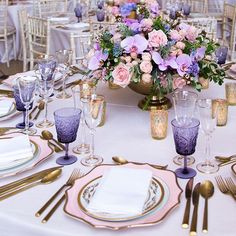 the table is set with gold and purple plates, silverware, and flowers in vases