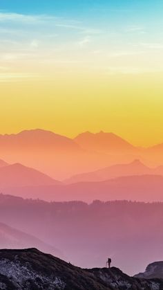 a person standing on top of a hill with mountains in the background at sunset or sunrise