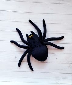 a black spider with yellow eyes sitting on top of a white wooden floor