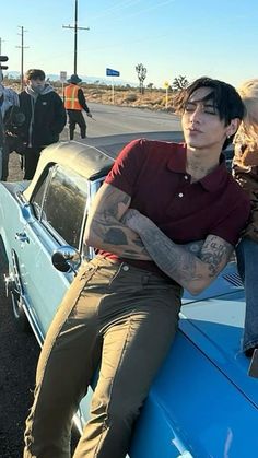 a man sitting on top of a blue car next to other people in the street