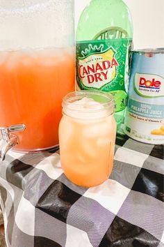 an orange drink sitting on top of a checkered table cloth next to two bottles