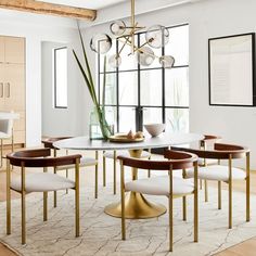 a dining room table with chairs and a chandelier hanging from the ceiling in front of a large window