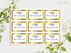 six olympic stickers with gold foil on them and white flowers in the foreground