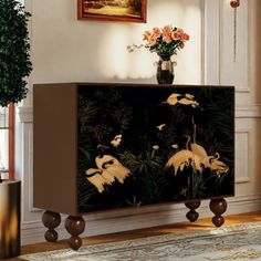 a cabinet with birds painted on it in a living room next to a potted plant