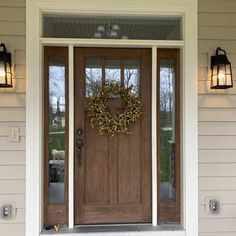 a front door with two lights and a wreath on it