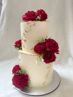 three tiered wedding cake with red roses on the top and bottom, sitting on a plate