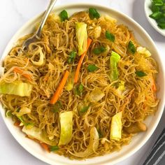 a white plate topped with noodles and veggies next to a bowl of chopsticks