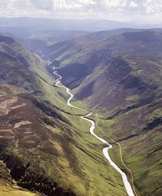 an aerial view of a valley with a river running through it and mountains in the background