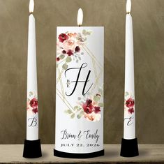 three candles with floral designs on them sitting next to each other in front of a wall