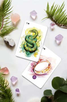 two cards with a green snake on one and a gold ring on the other, surrounded by crystals