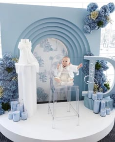 a baby sitting in a high chair surrounded by blue candles and flowers on a table