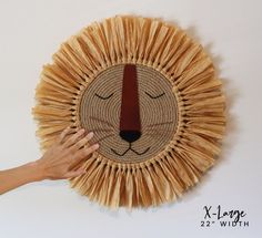 a hand is touching the face of a woven wall decoration with straws on it