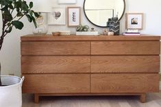 a wooden dresser sitting next to a potted plant in a room with pictures on the wall