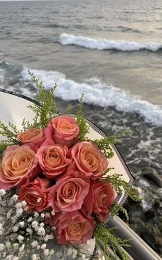 a bouquet of pink roses sitting on top of a white chair next to the ocean