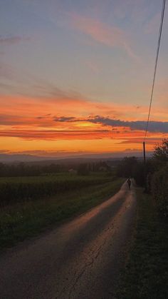 a person riding a bike down a dirt road at sunset with the sun setting in the distance