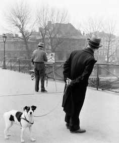 an old black and white photo of a man walking his dog on a leash with two other men in the background