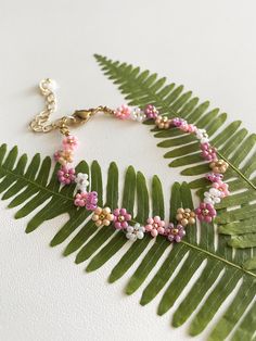 a green leaf with pink and white flowers on it's end is next to a gold chain