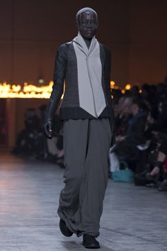 a model walks down the runway in grey pants and black jacket with white collared shirt