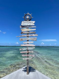 there is a wooden sign that has many different signs on it in front of the water