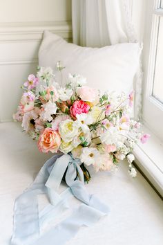 a bouquet of flowers sitting on top of a bed next to a pillow and window