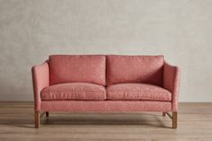 a pink couch sitting on top of a hard wood floor next to a white wall