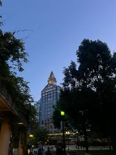 people are sitting on benches in the park at dusk with tall buildings in the background