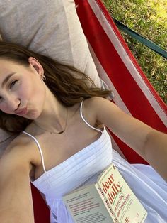 a woman laying in a hammock with a book on her lap and looking at the camera